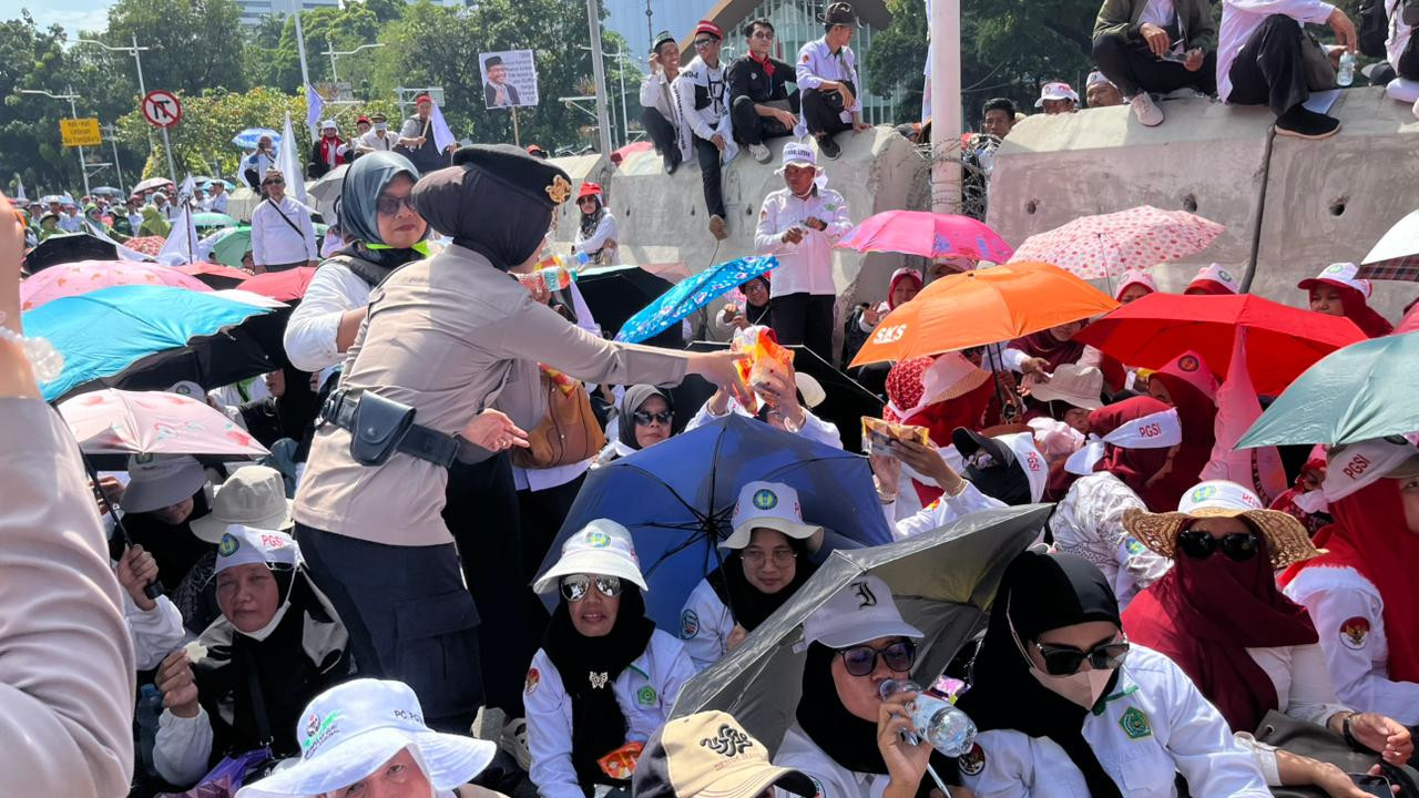 Polisi Bagikan Air Mineral dan Roti kepada Massa Aksi Damai Guru di Silang Selatan Monas